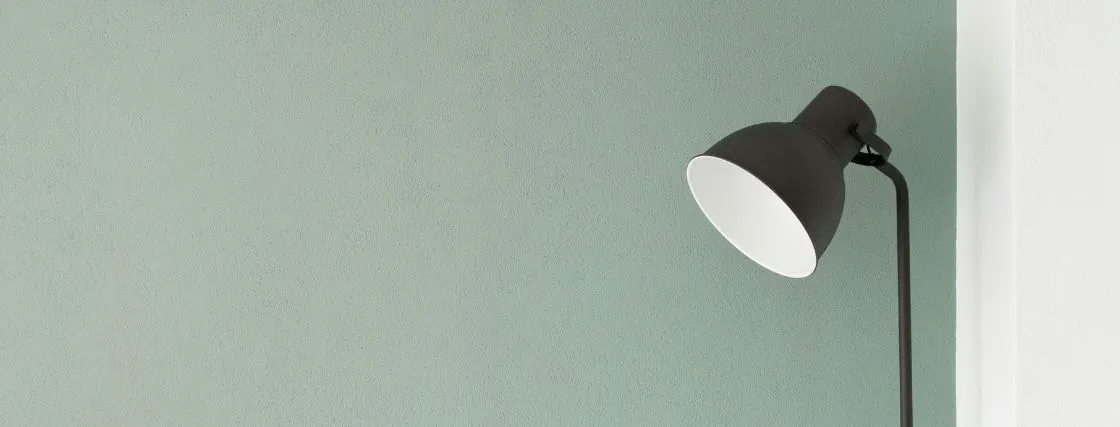 Eine schwarze Stehlampe steht vor einer mintgrünen Wand